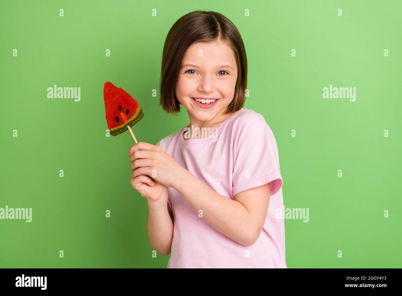 Photo of young cheerful little girl happy positive smile hold sweets stick lollipop caramel isolated over green color background Stock Photo