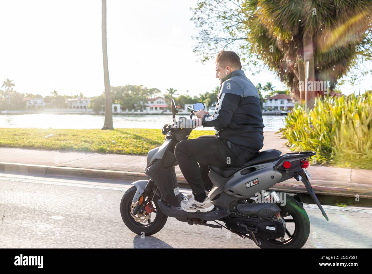Miami Beach, USA - January 19, 2021: Young man riding motorcycle scooter in danger of accident while using smartphone mobile phone on city street road Stock Photo