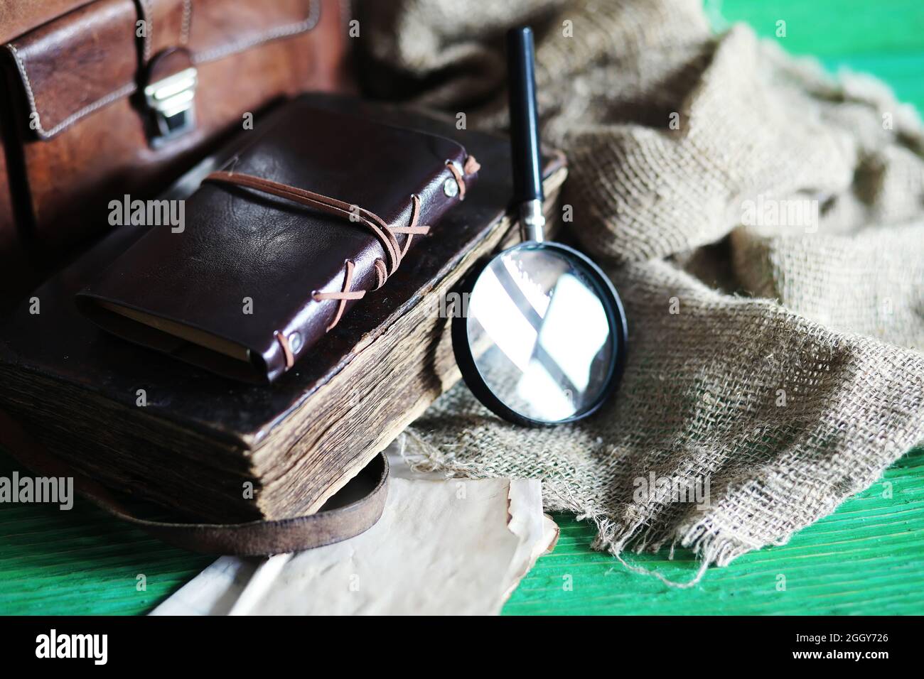 Old leather bag with a magnifying glass on a brown traveler wooden table background copy space. Stock Photo