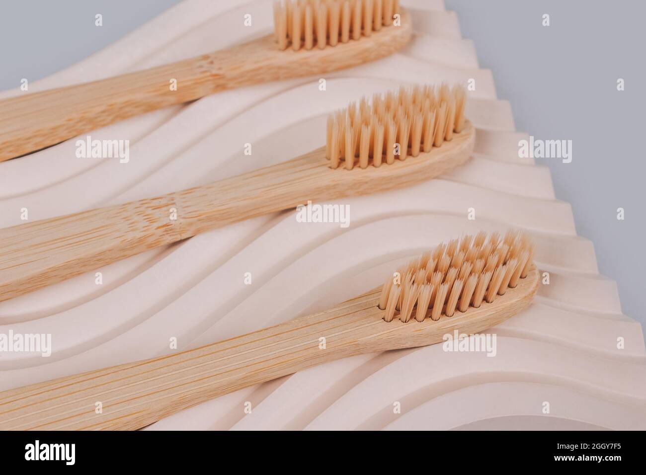 Set of natural bamboo toothbrushes on biege plaster mold against gray background with copy space