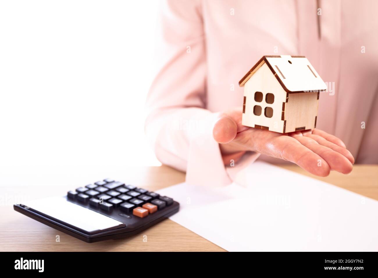 Woman holds model of house on hand, on the table lies a contract and calculator Stock Photo