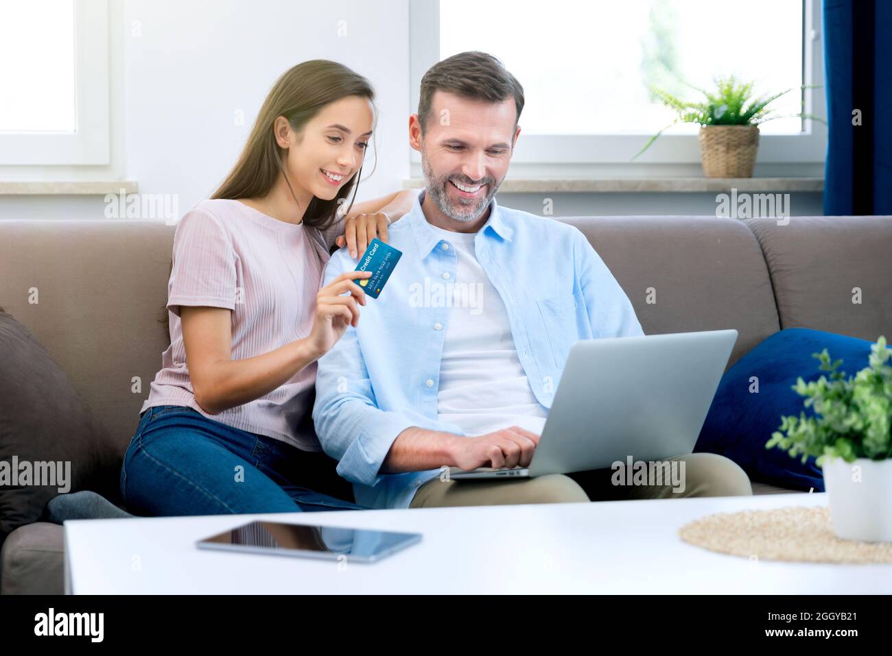 Happy couple couple e-shopping on internet. Woman using credit card, man with laptop Stock Photo