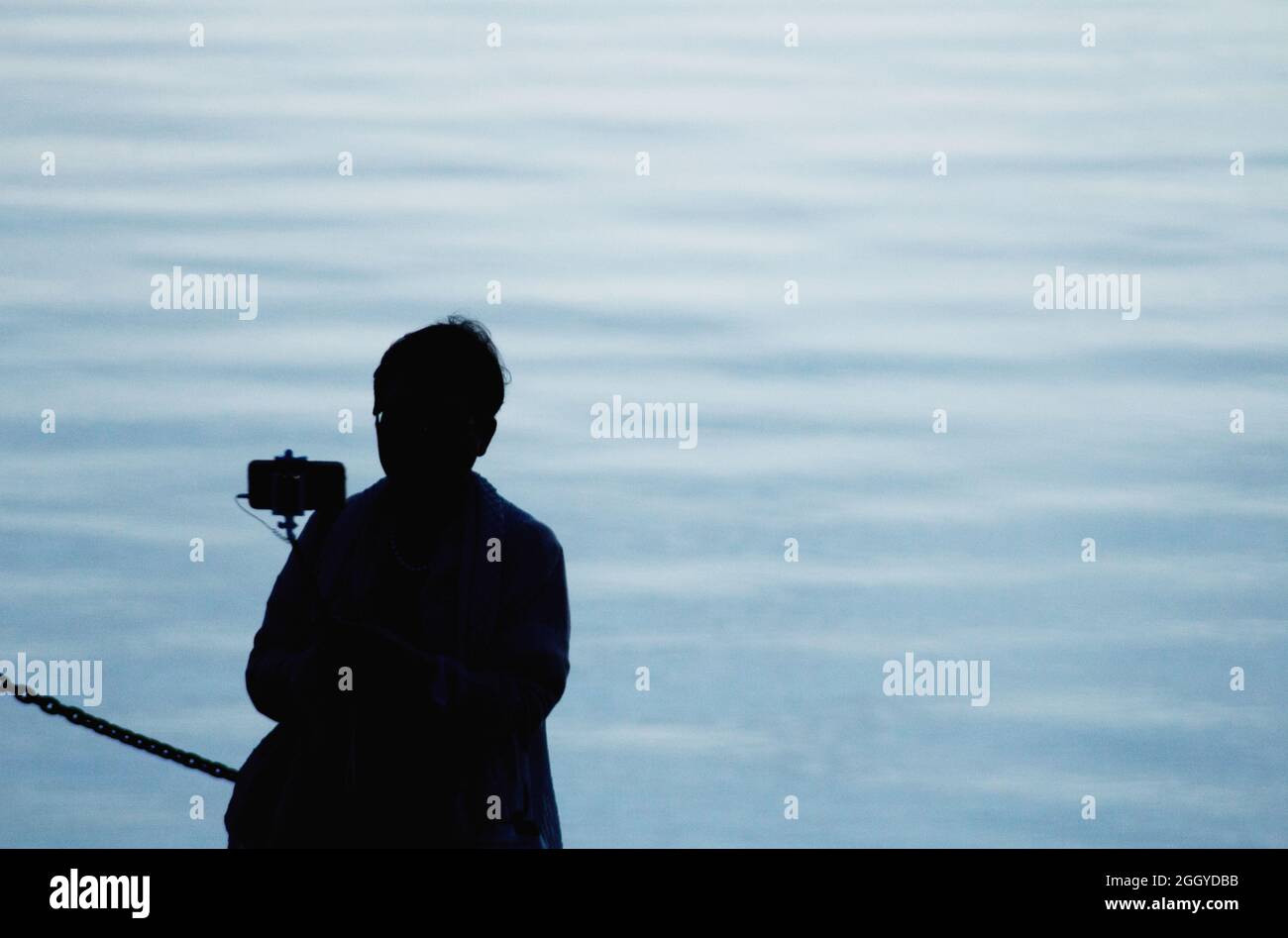 Silhouette of woman taking photograph of water at dusk, Victoria BC Canada. Stock Photo