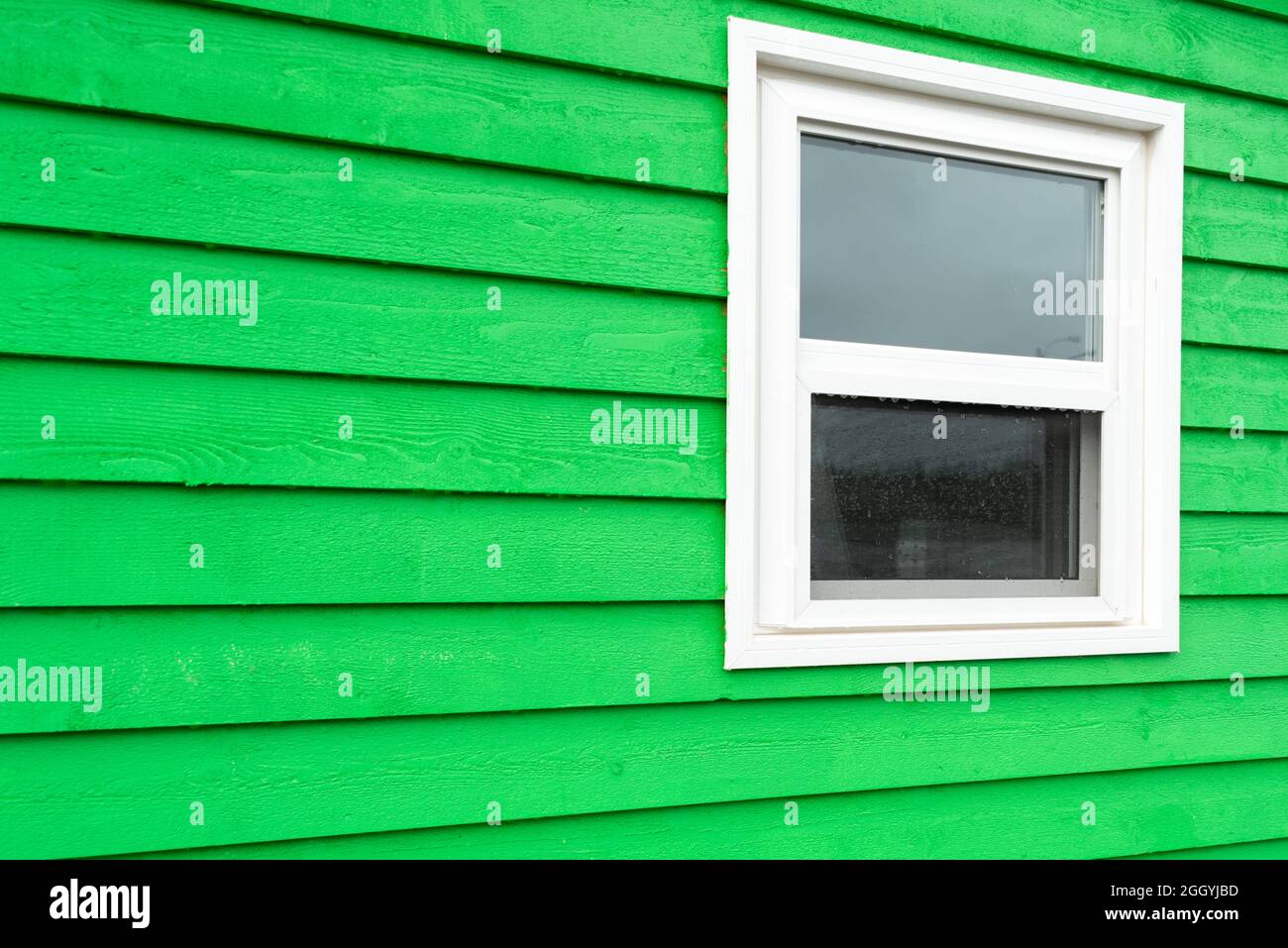 The exterior of a bright green narrow wooden horizontal clapboard wall of a house. The trim on