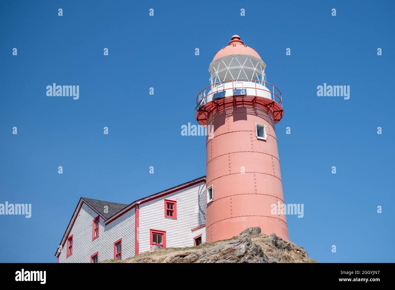 The top of a vintage lighthouse tower with a round red metal roof.  In the center of the lighthouse is a vintage lamp made of multiple pieces of glass Stock Photo