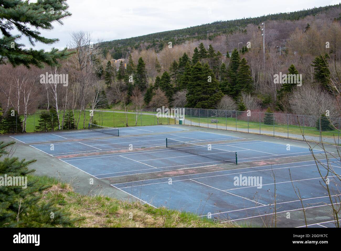 An outdoor tennis court with blue paint, white lines, and a black mesh tennis net. The edge of the court has white lines. Stock Photo