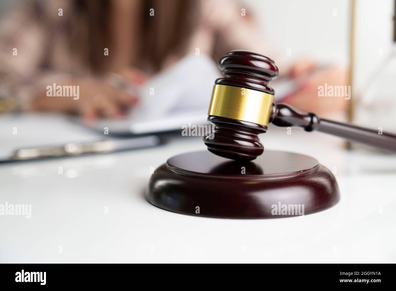 Young female lawyer during work in chamber. Gavel and hourglass on the white table. Stock Photo