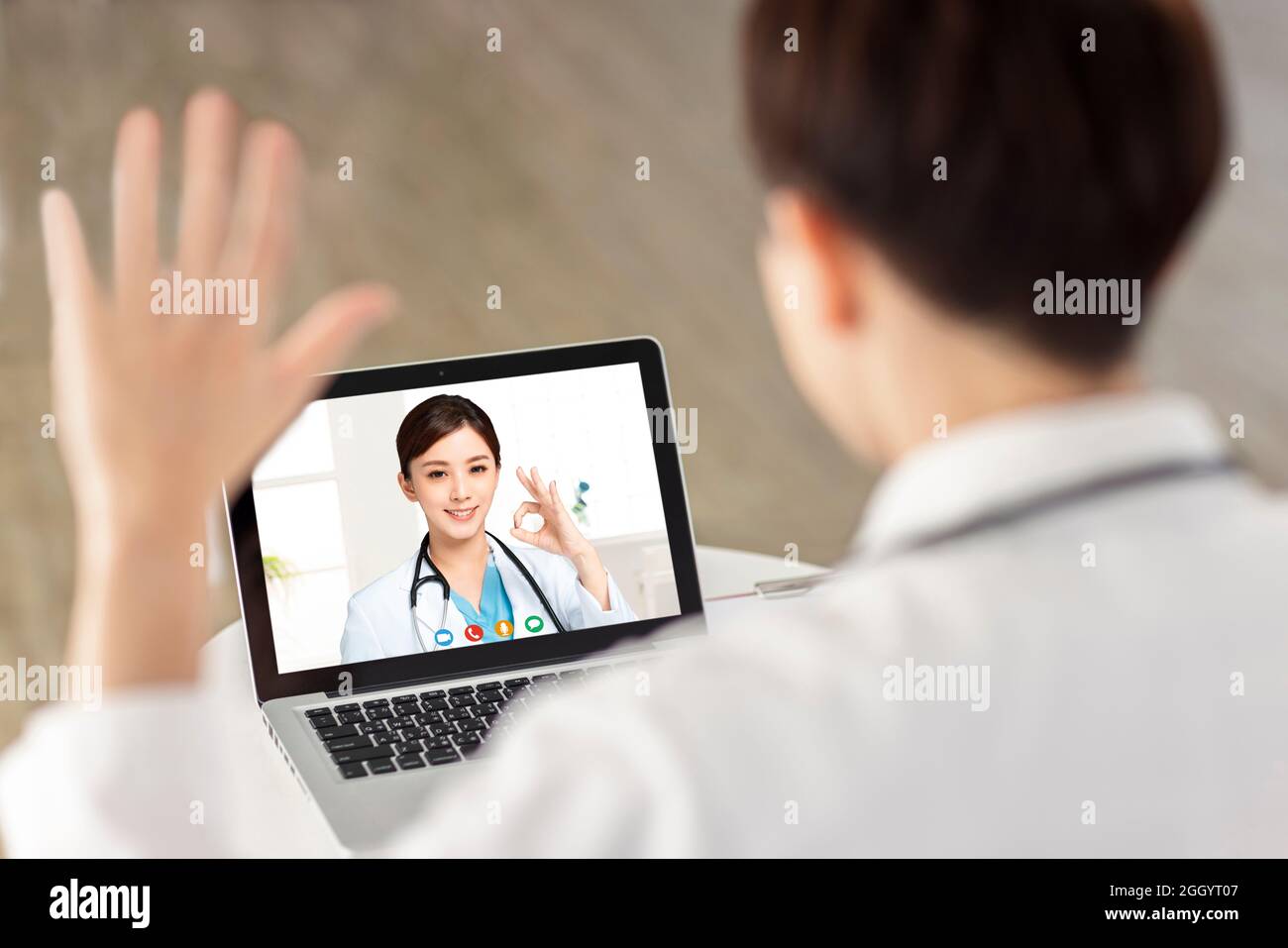 Back view of doctor making video call with his colleague.Smiling doctor showing ok gesture. Stock Photo