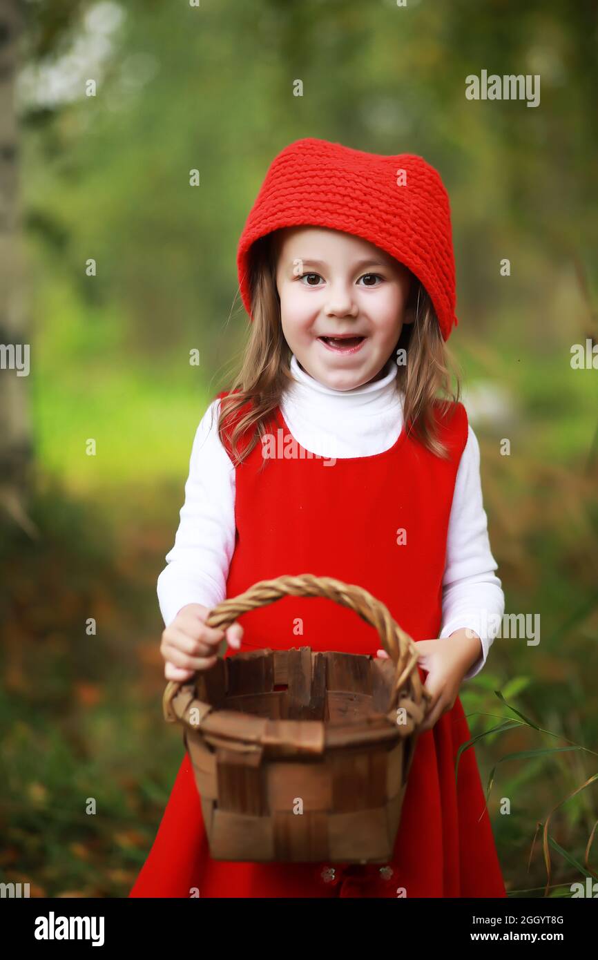 A little girl in a red hat and dresses is walking in the park. Cosplay ...