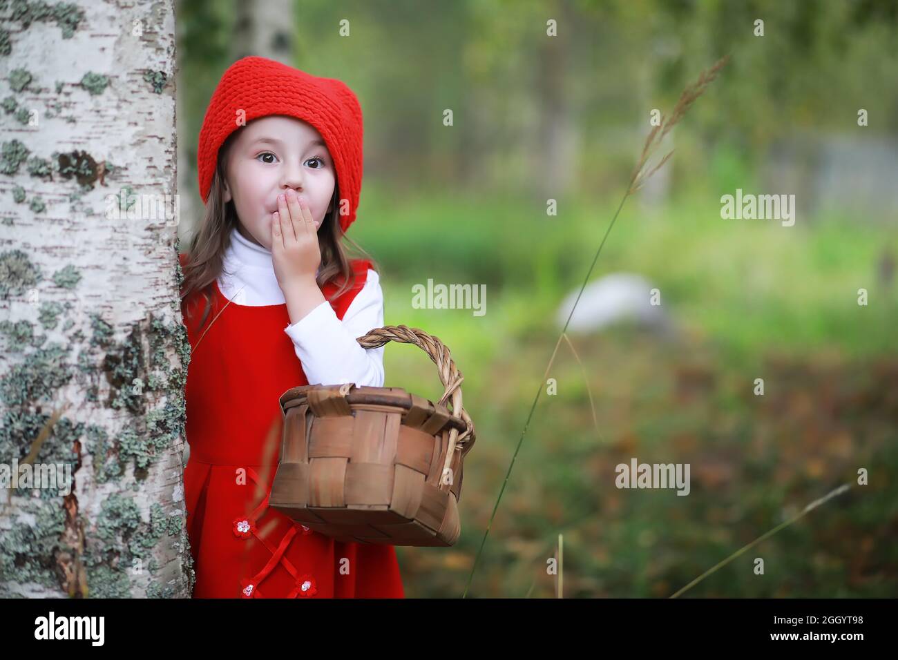 A little girl in a red hat and dresses is walking in the park. Cosplay ...