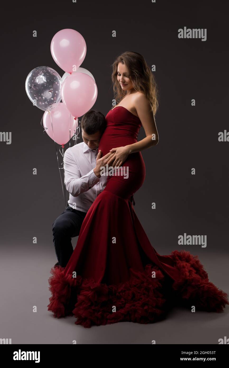 Smiling young pregnant couple touching tummy against gray background Stock Photo