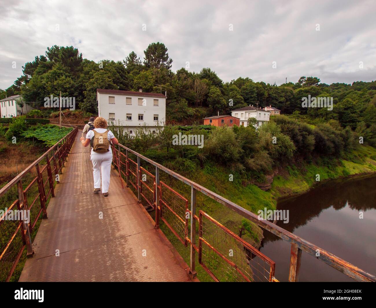 Pilgrim woman passing over a stone bridge with two yellow arrows for orientation on the route of the Camino de Santiago as it passes through Galicia. Stock Photo