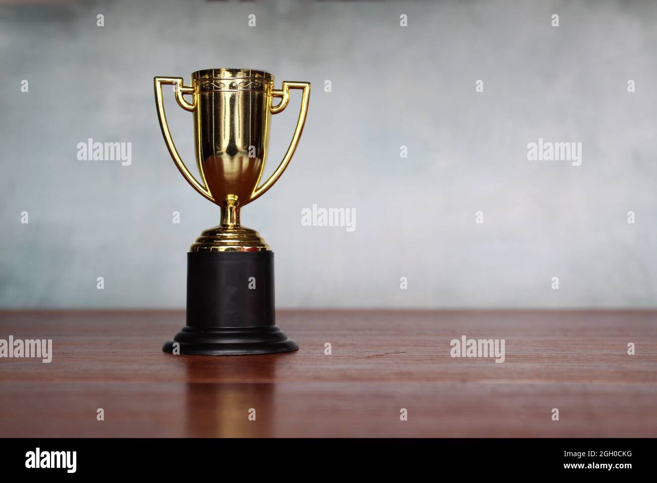 Gold trophy cup on table against concrete wall with copy space Stock Photo
