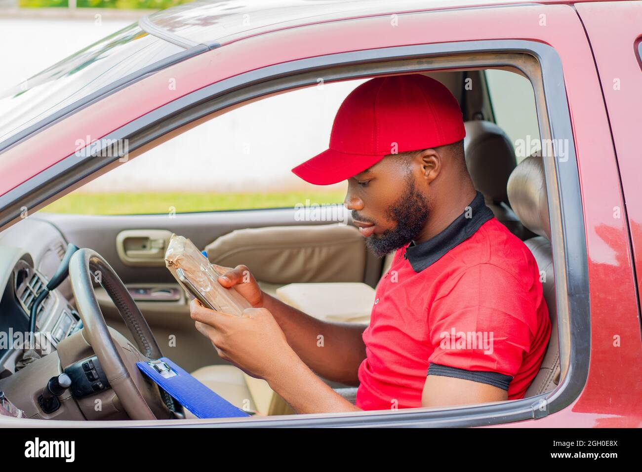 african delivery worker in a car using his phone Stock Photo