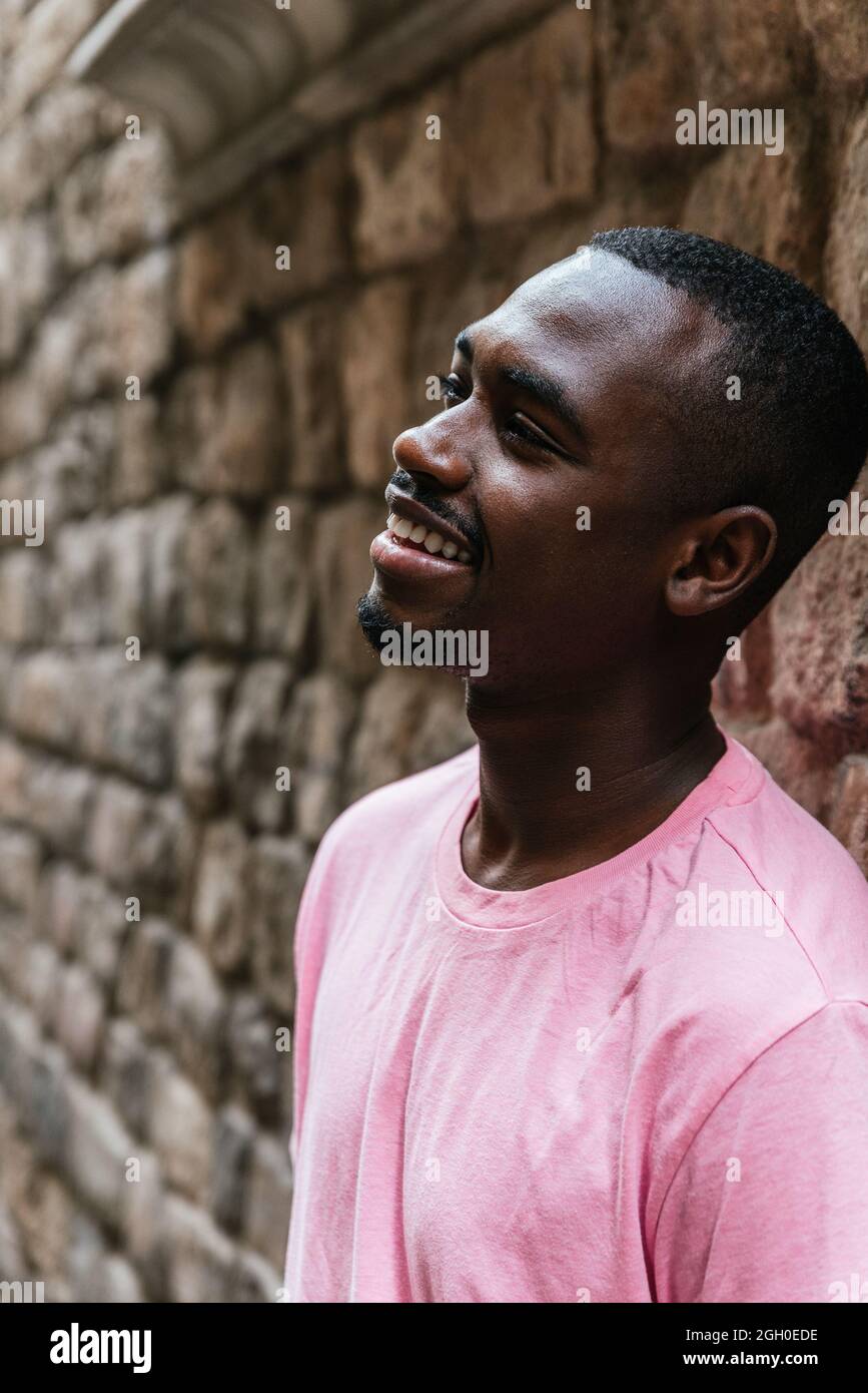 vertical portrait of an afro american young man. He is looking to one side near a stone wall Stock Photo