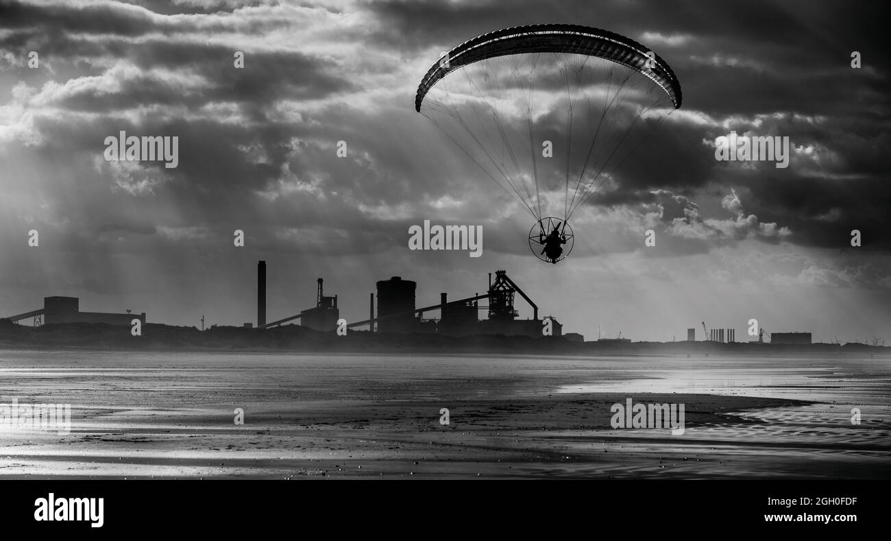 Powered paragliding along Coatham beach with the former Redcar Steelworks in the distance. Redcar, Cleveland, North Yorkshire, England, UK Stock Photo