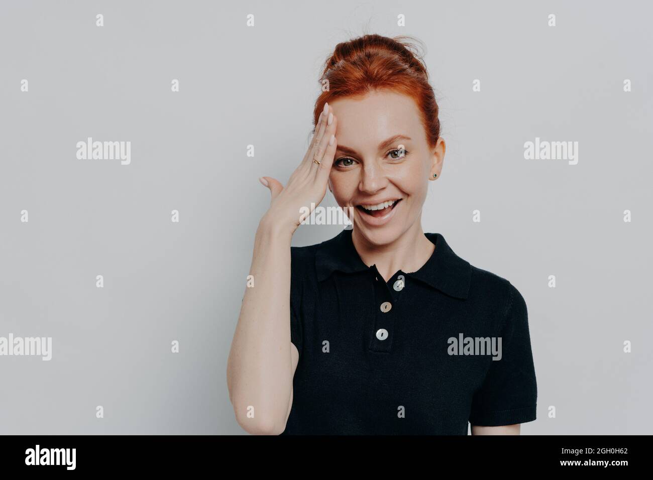 Pretty red-haired woman with hair in bun forgetting something, isolated on grey background Stock Photo