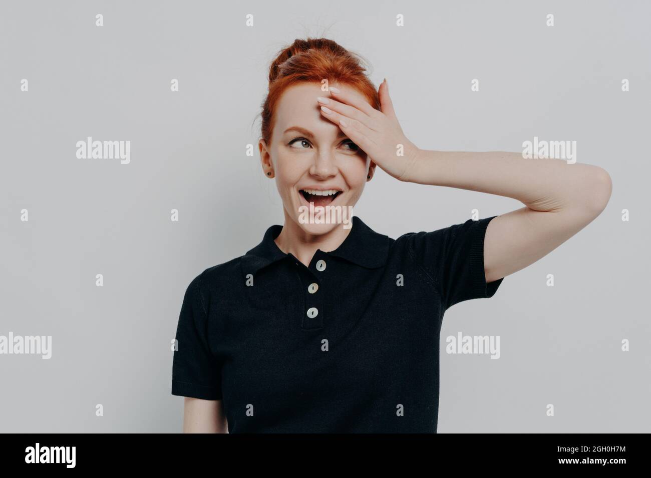 Happy young redhead woman with opened mouth touching her forehead with hand Stock Photo