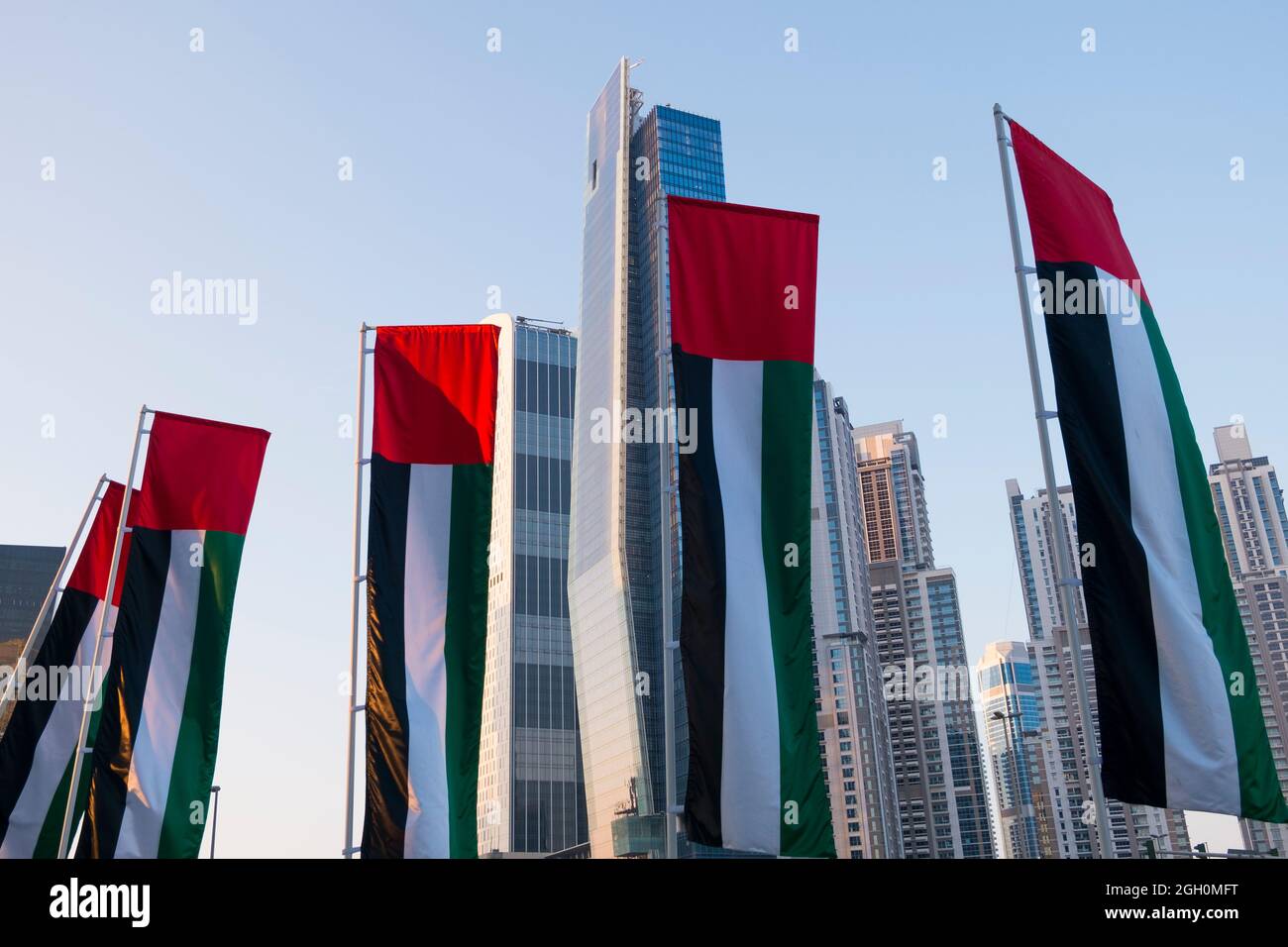 UAE flags flying on poles with tall buildings in the new downtown section. In Dubai, United Arab Emirates. Stock Photo