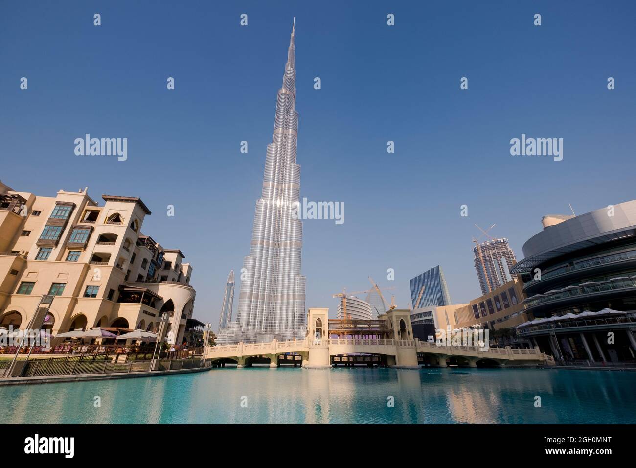 The skyscraper Burj Khalifa in the background of new mixed development, pedestrian bridge and lake. In Dubai, United Arab Emirates. Stock Photo
