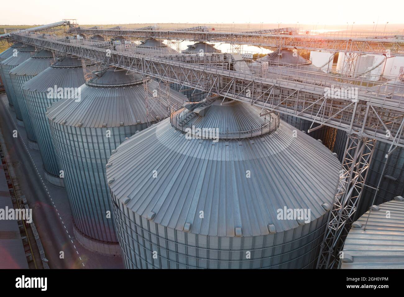 Grain terminals of modern sea commercial port. Silos for storing grain in rays of setting sun, top view from quadcopter. Industrial background. Logist Stock Photo