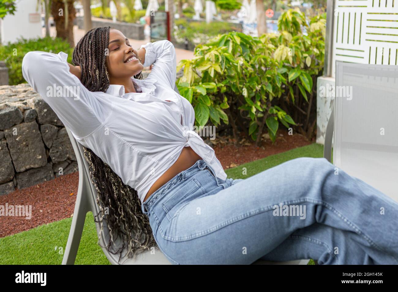 Adult woman relaxing outside leaning back in a chair with her hands clasped  behind her neck with eyes closed. African american woman enjoying the day  Stock Photo - Alamy