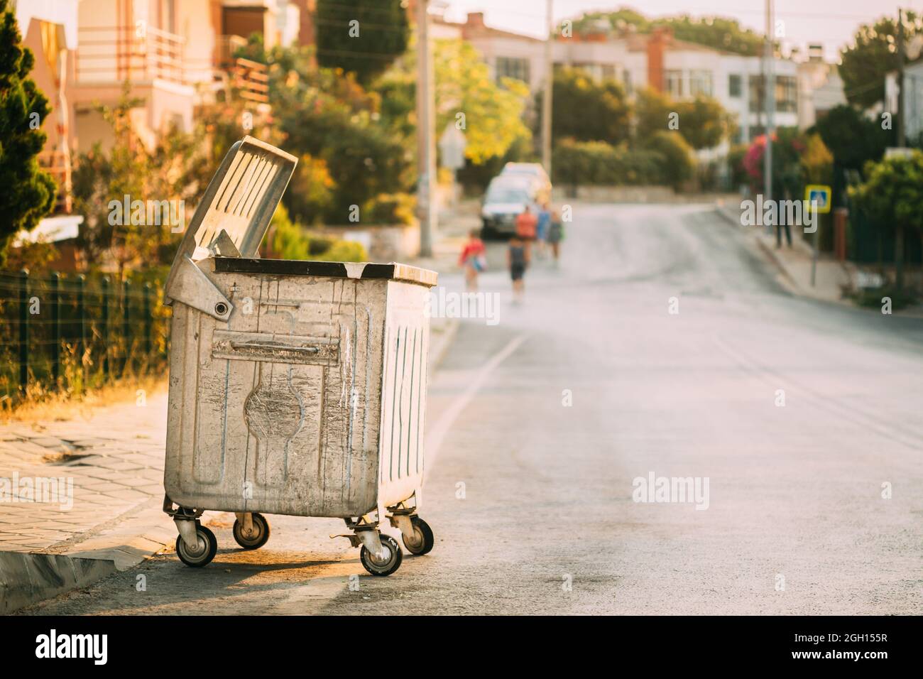 Metal Waste Container On Wheels In Street During Summer Sunny Evening