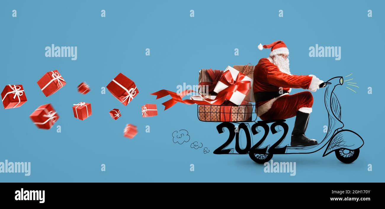 Santa Claus on scooter delivering Christmas or New Year 2022 gifts at blue background Stock Photo