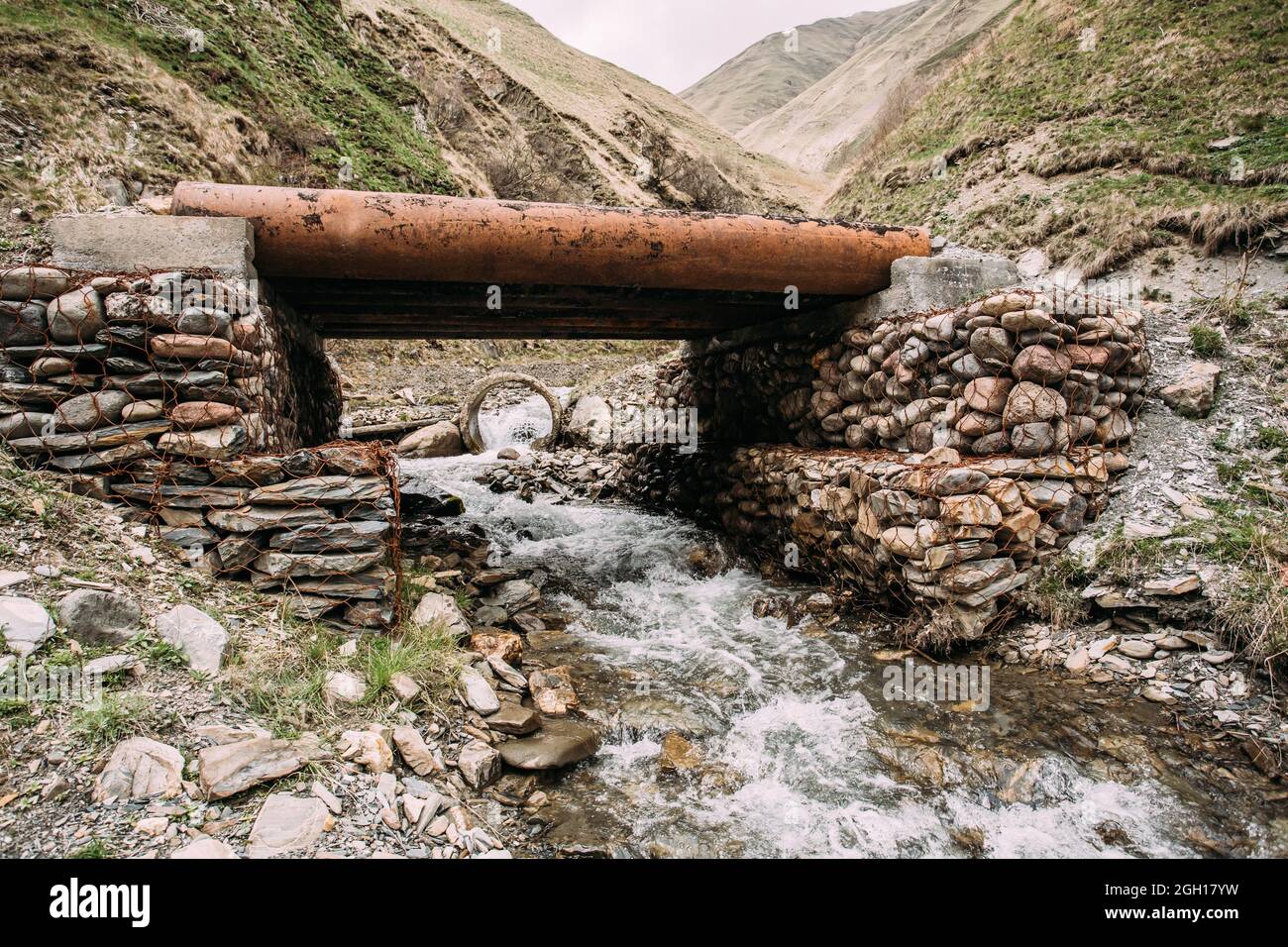 Small Bridge Through Terek River In In Truso Gorge, Kazbegi District, Mtskheta-mtianeti Region, Georgia. Spring Or Summer Season. Stock Photo