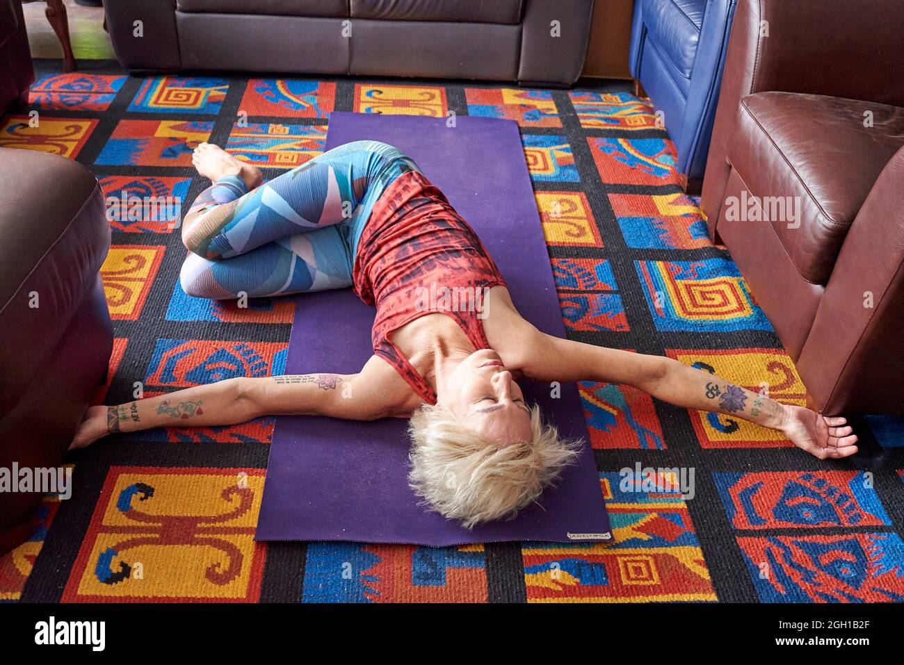 A woman, 60+ years old, moves her legs to her side and spreads her arms out  as she practices yoga in her apartment home, Windsor, Ontario, Canada Stock  Photo - Alamy