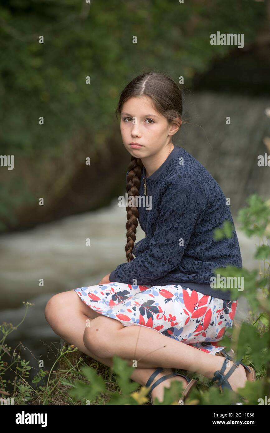Young girl with a long plait sitting next to a waterfall, France, Europe. Stock Photo