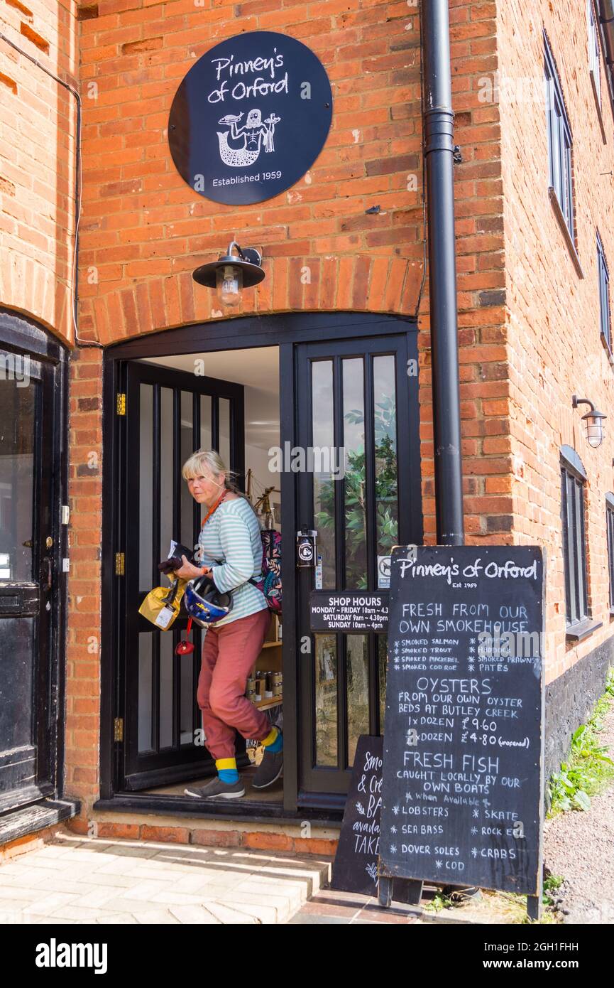 A wonam emerging from Pinney's of Orford fish smokehouse shop, with purchases,  Orford, Suffolk, England Stock Photo