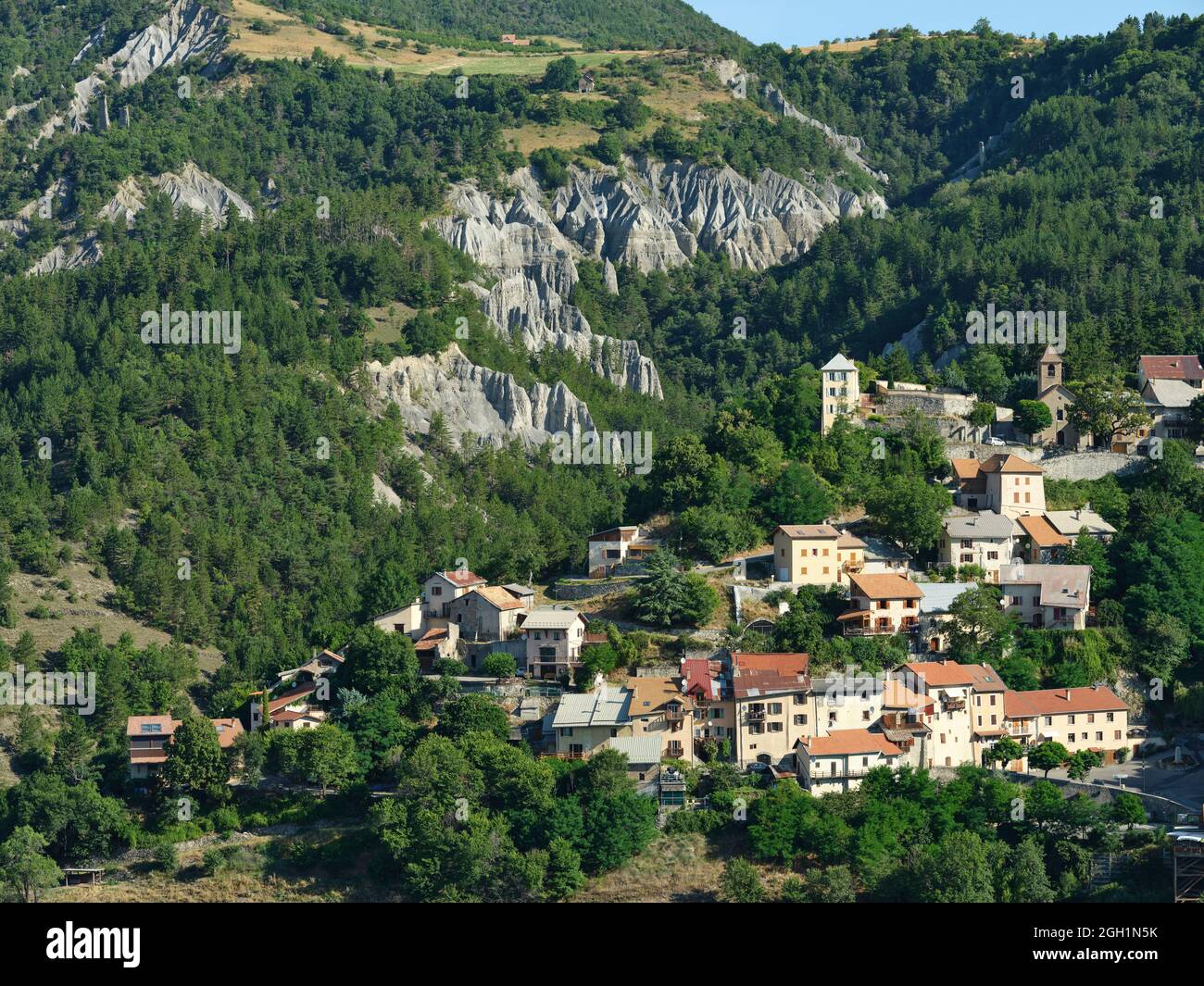 AERIAL VIEW. Village of Théus with its background of badlands and numerous hoodoos. Durance Valley, Hautes-Alpes, France. Stock Photo