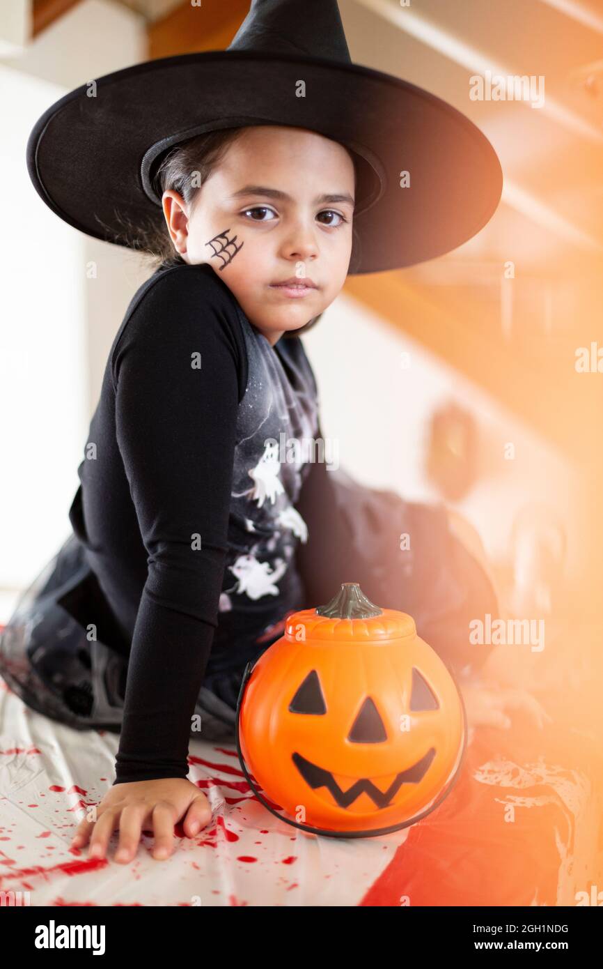 Portrait of caucasian little girl in witch costume next to a pumpkin ...