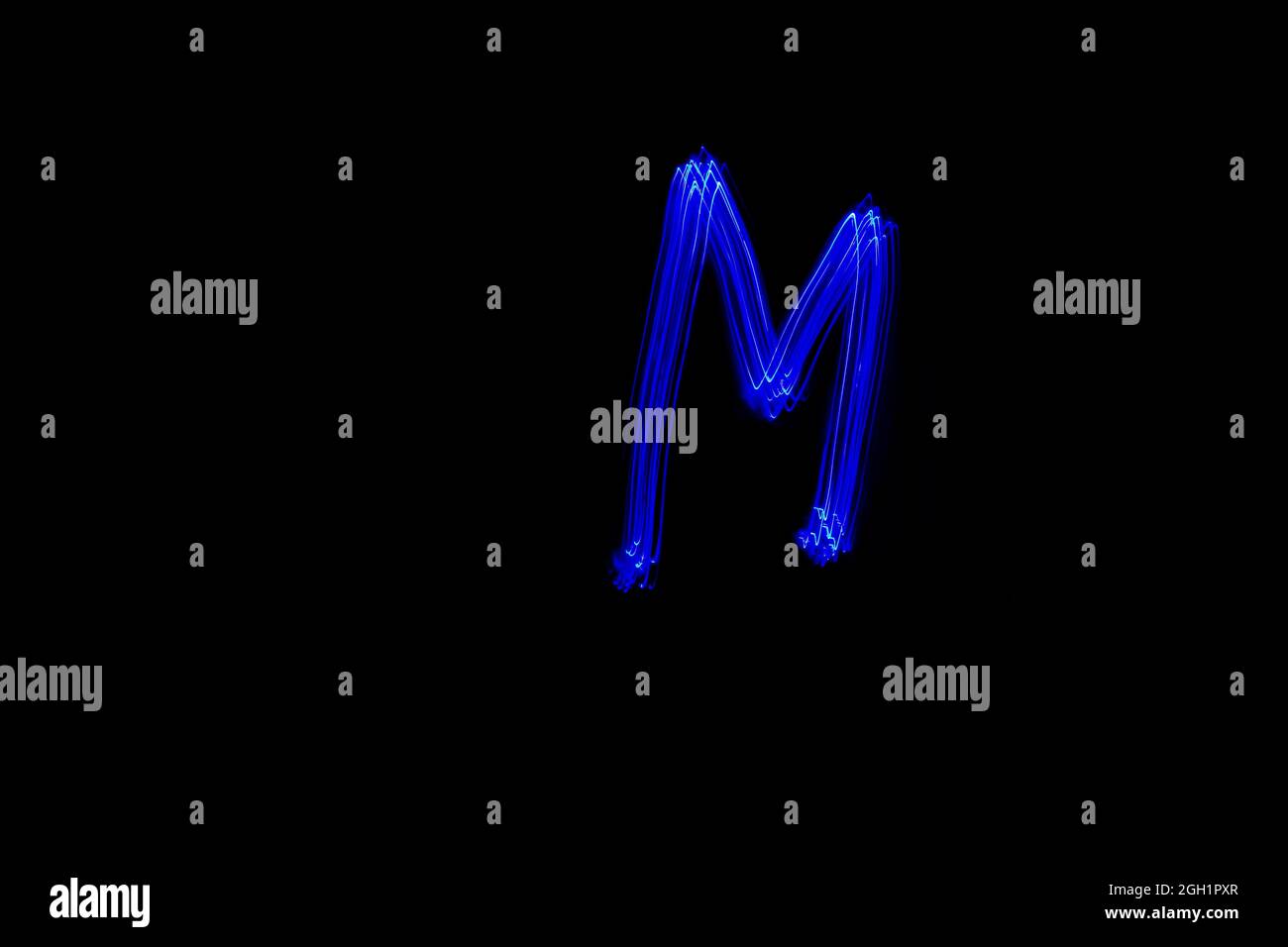 Letter M. Light painting alphabet. Long exposure photography. Drawn letter M with blue lights against black background. Stock Photo