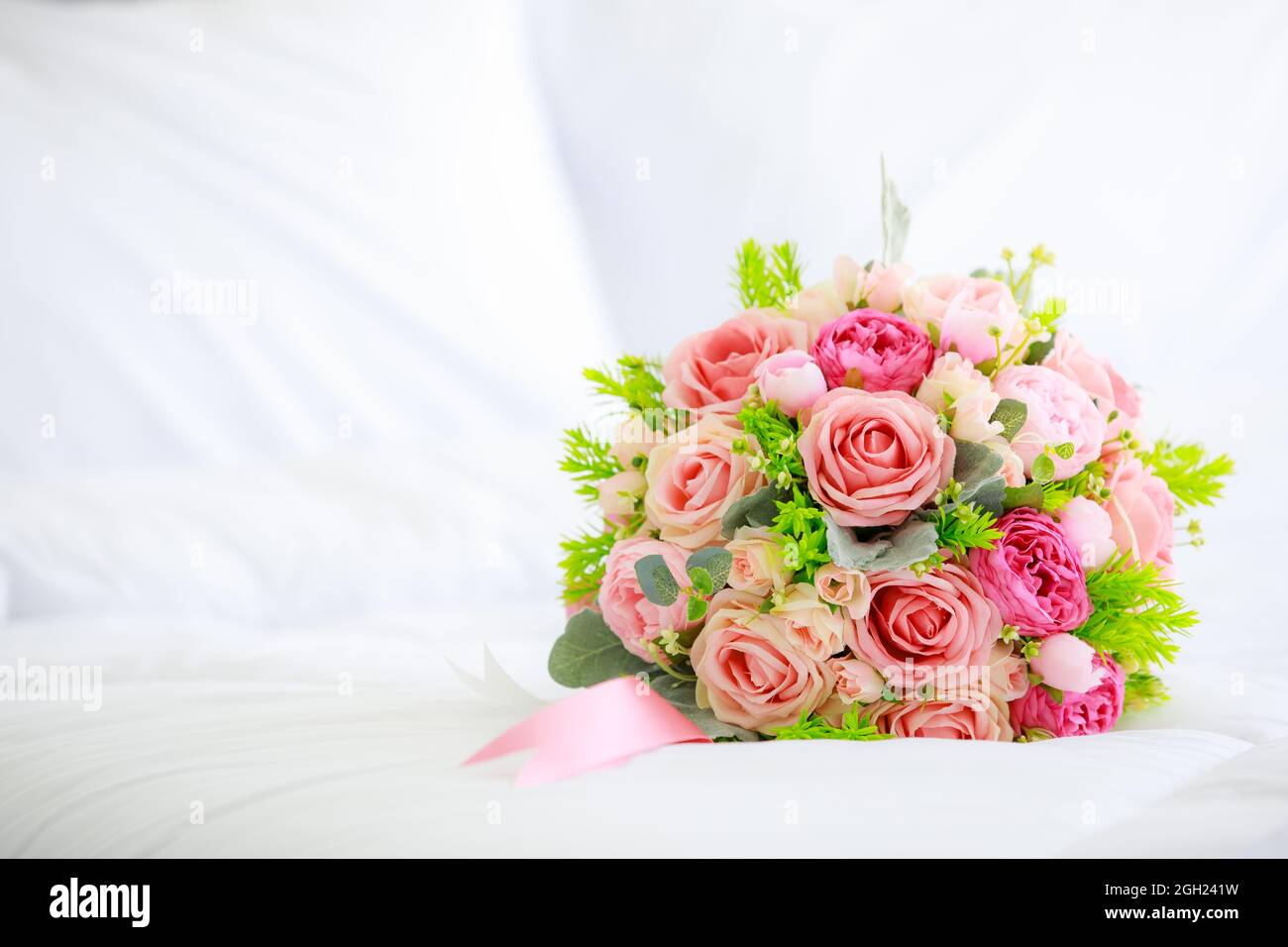 A bouquet bunch of colorful fake fabric flowers on white bed cover with copy spce. Stock Photo