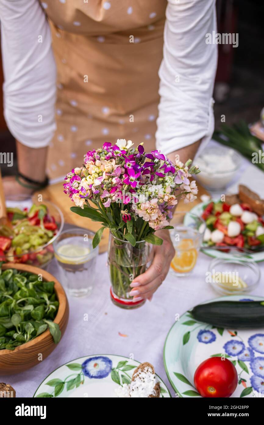 Woman arranging dining table with bouquet of flowers. Setting table for garden party Stock Photo