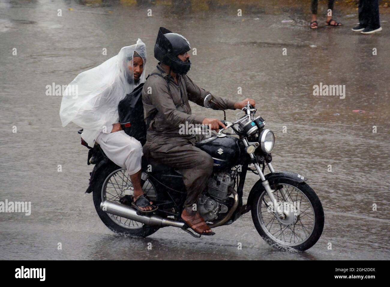 Commuters hold umbrella and plastic sheets over their head to save themselves from rain move toward their destination during heavy downpour of monsoon season, at Saddar area of Karachi on Saturday, September 04, 2021. Stock Photo