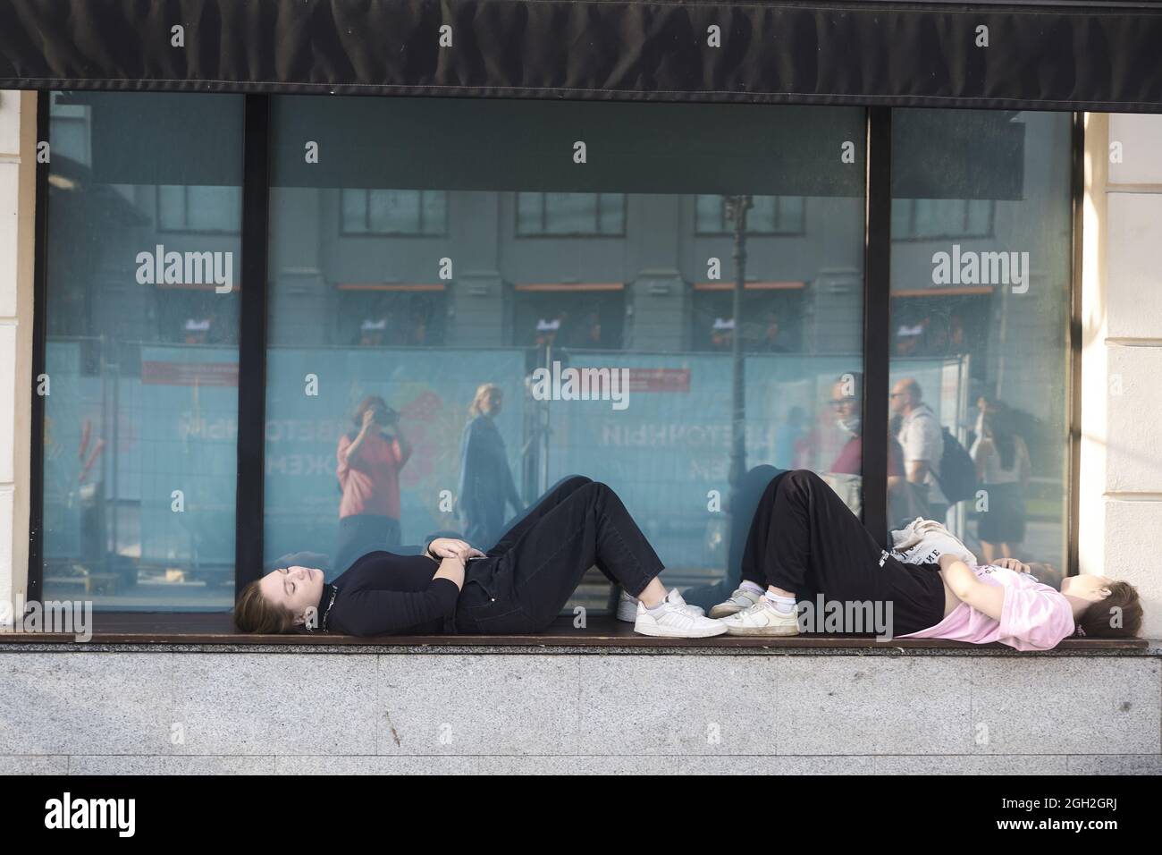 Moscow, Russia - 31 August, 2021, Two girls lie on the windowsill of a large window, resting. Kamergersky lane Stock Photo