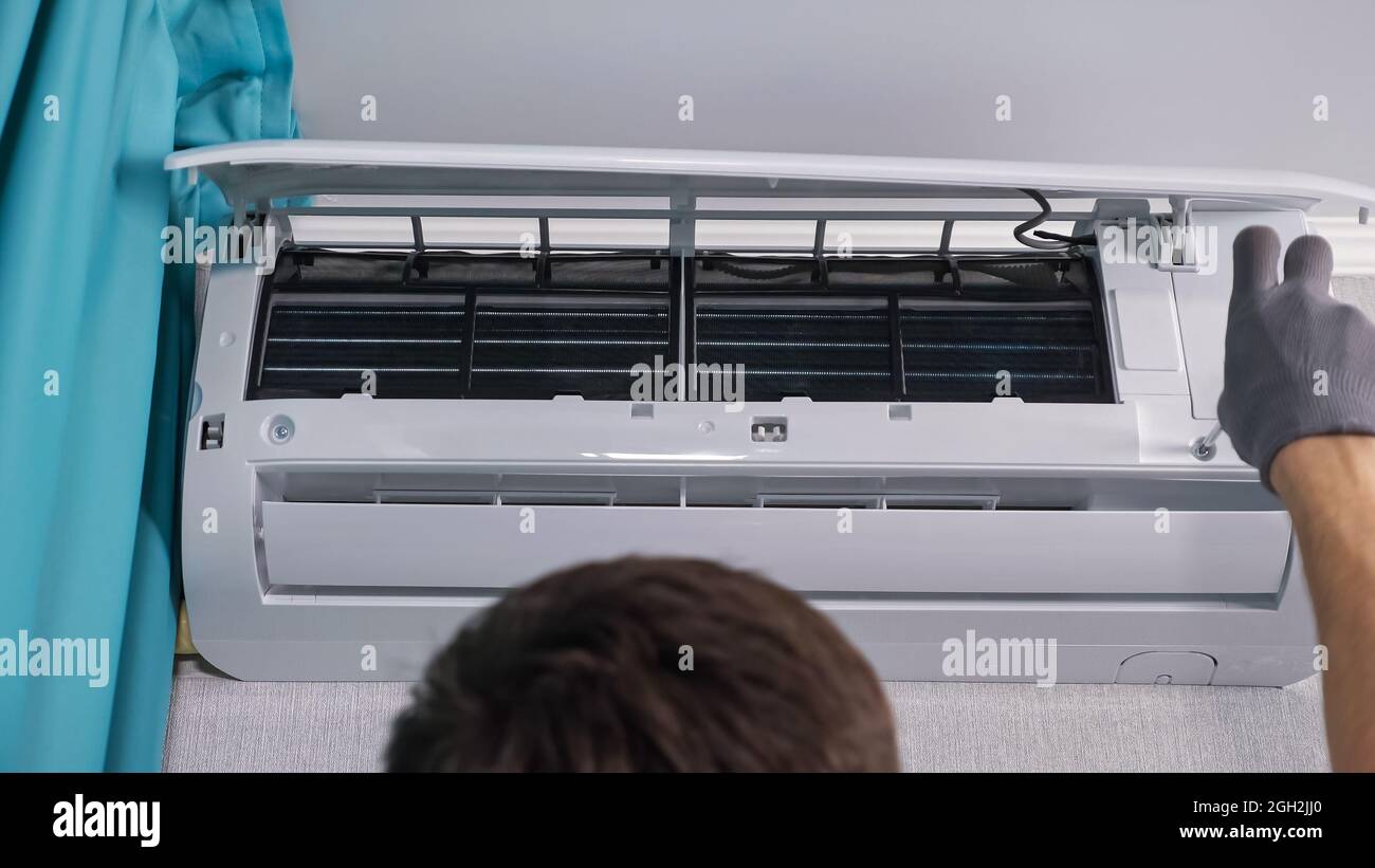 Man worker removes screws from air conditioner under ceiling Stock