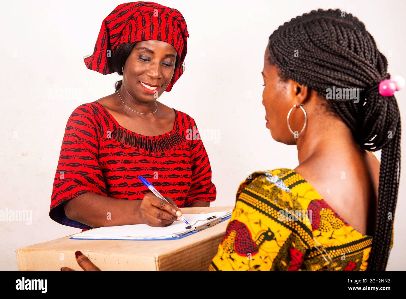 beautiful african woman standing in traditional dress on white background smiling signing a document after receiving an online package. Stock Photo