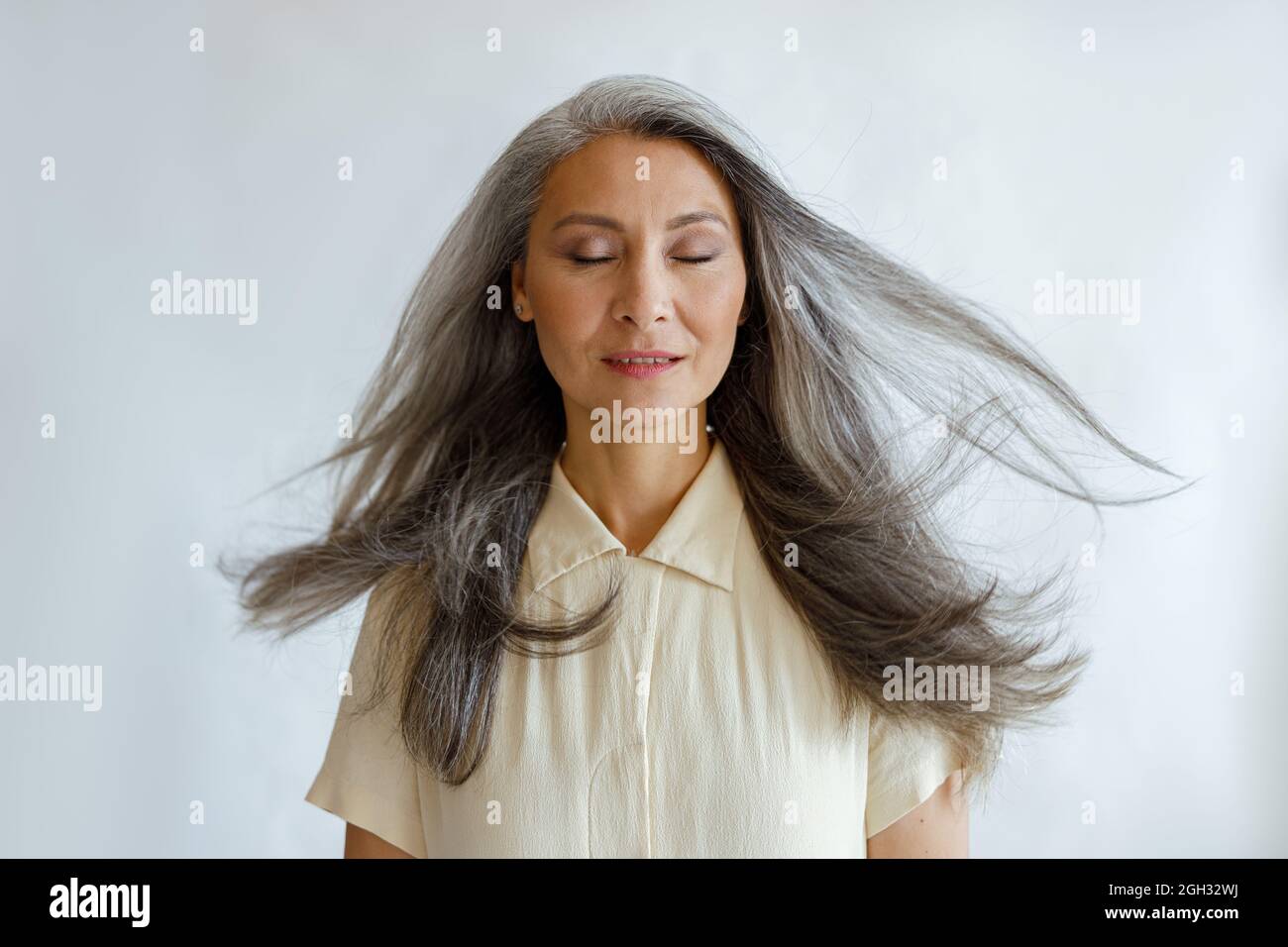 Pretty tranquil Asian woman with flying silver hair stands on light grey  background Stock Photo - Alamy