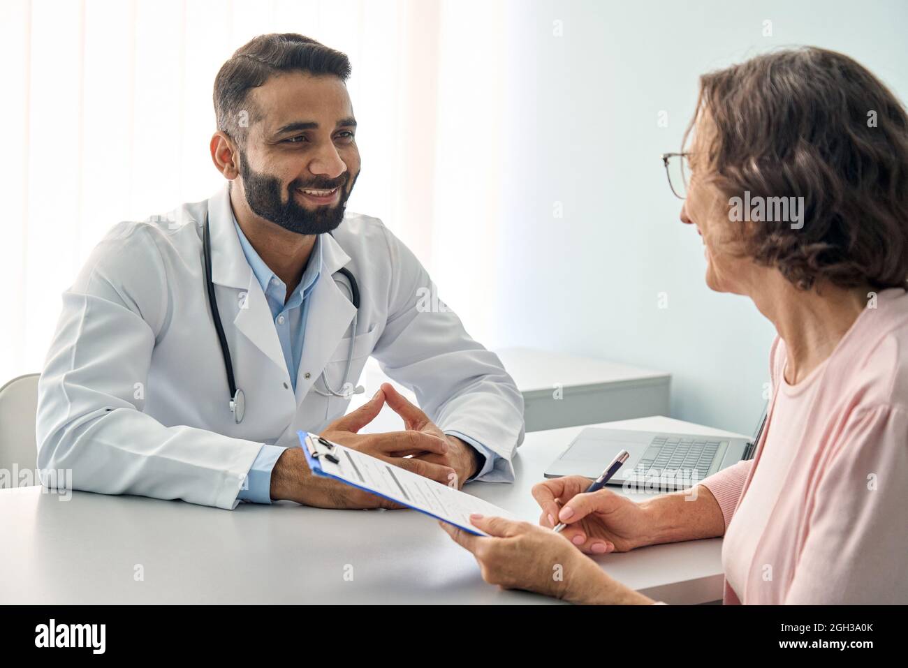Happy Indian male doctor consulting senior patient filling medical form. Stock Photo