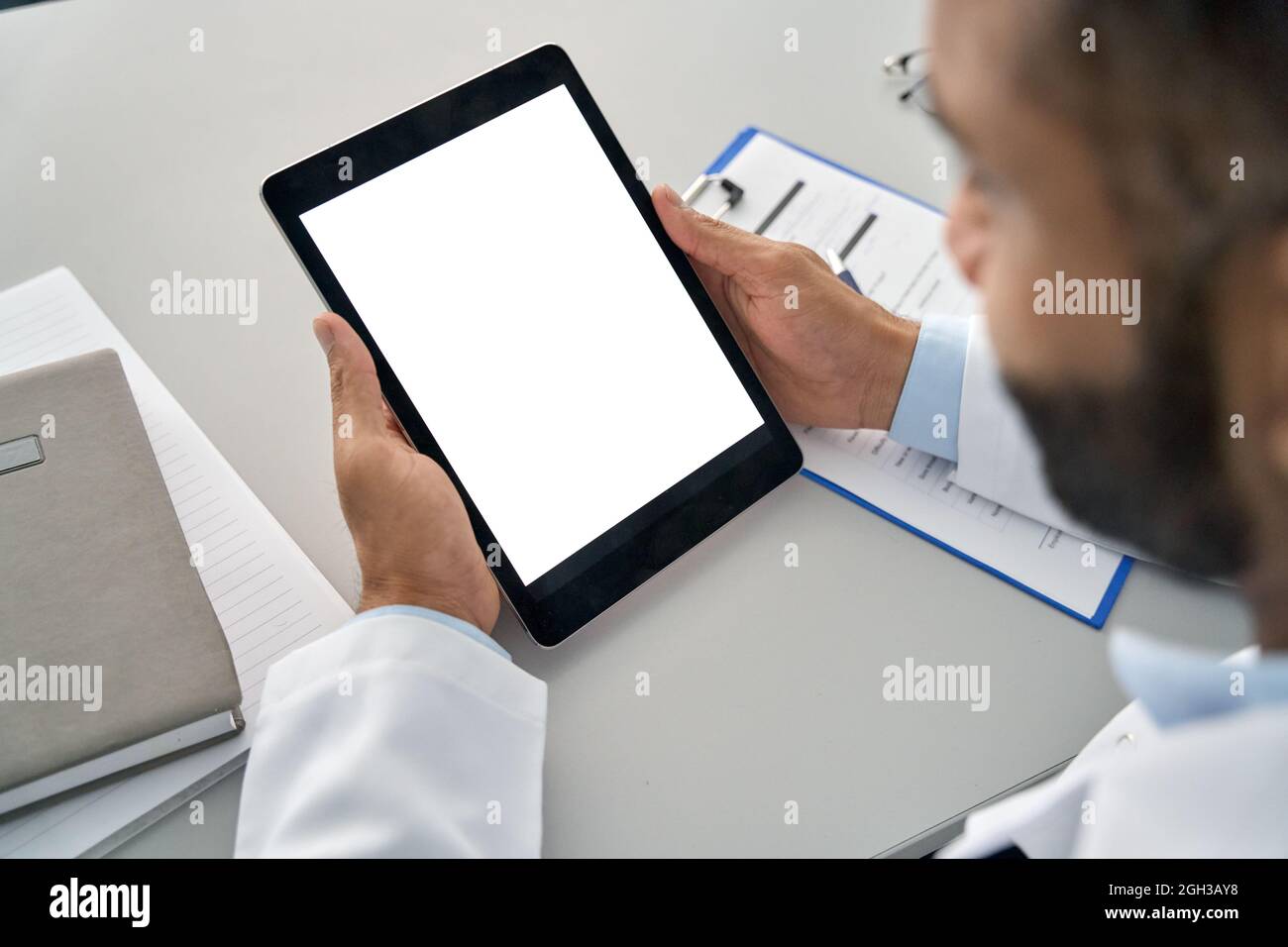 Male doctor holding digital tablet in hands looking at white mockup screen. Stock Photo