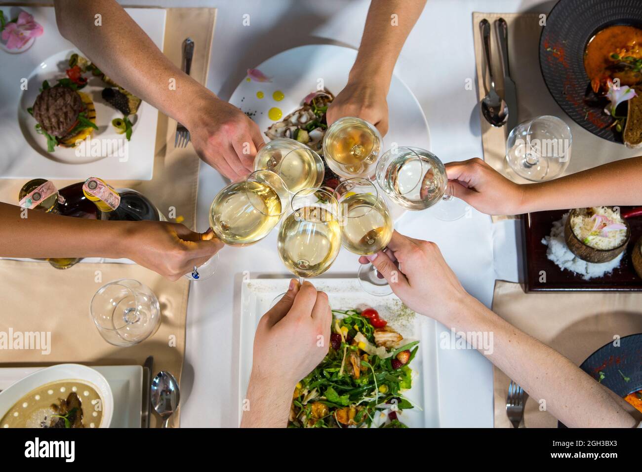 People clink glasses over a served table. Hands with glasses of wine