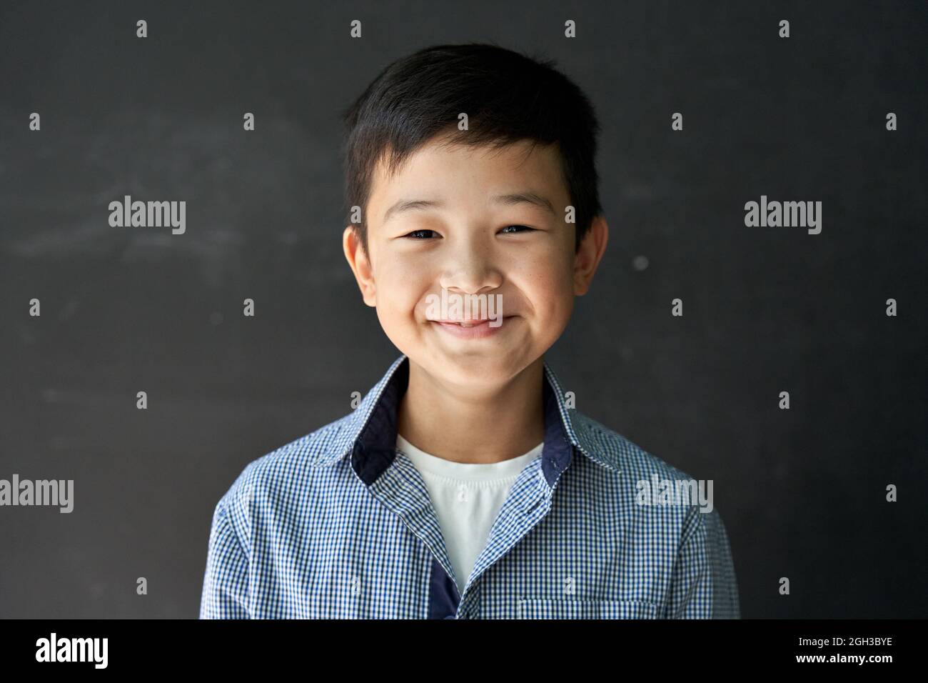 Happy Asian kid boy school student looking at camera at blackboard background. Stock Photo