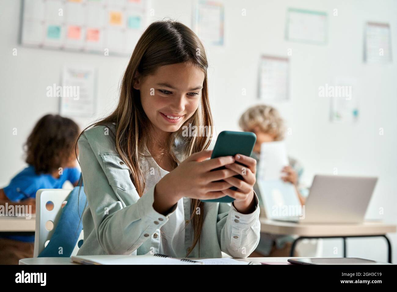 Happy latin hispanic kid girl school student using smartphone in classroom. Stock Photo