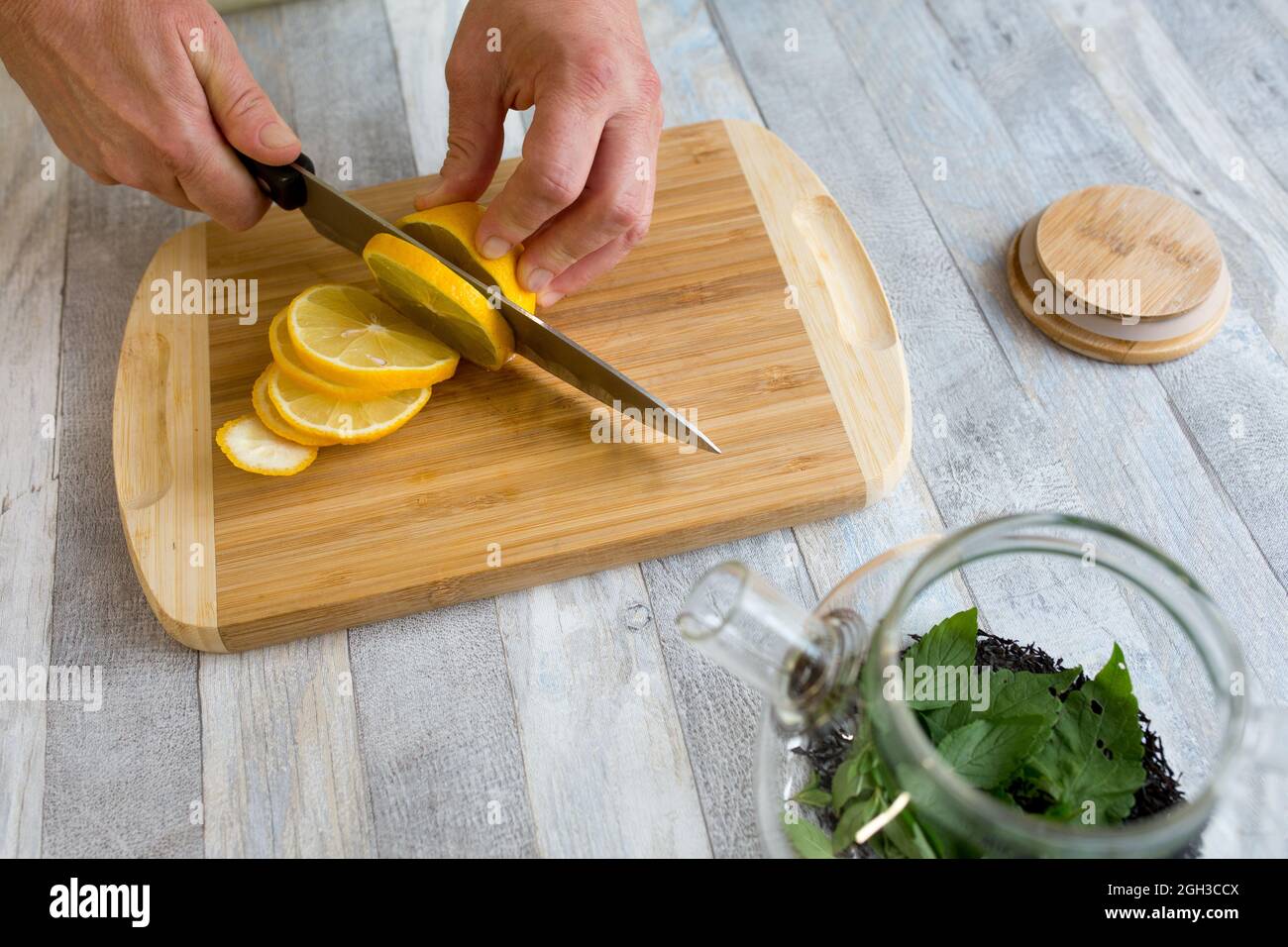 https://c8.alamy.com/comp/2GH3CCX/a-woman-cuts-a-lemon-on-a-wooden-kitchen-board-with-a-sharp-large-knife-healthy-food-concept-the-process-of-making-tea-with-mint-and-lemon-2GH3CCX.jpg