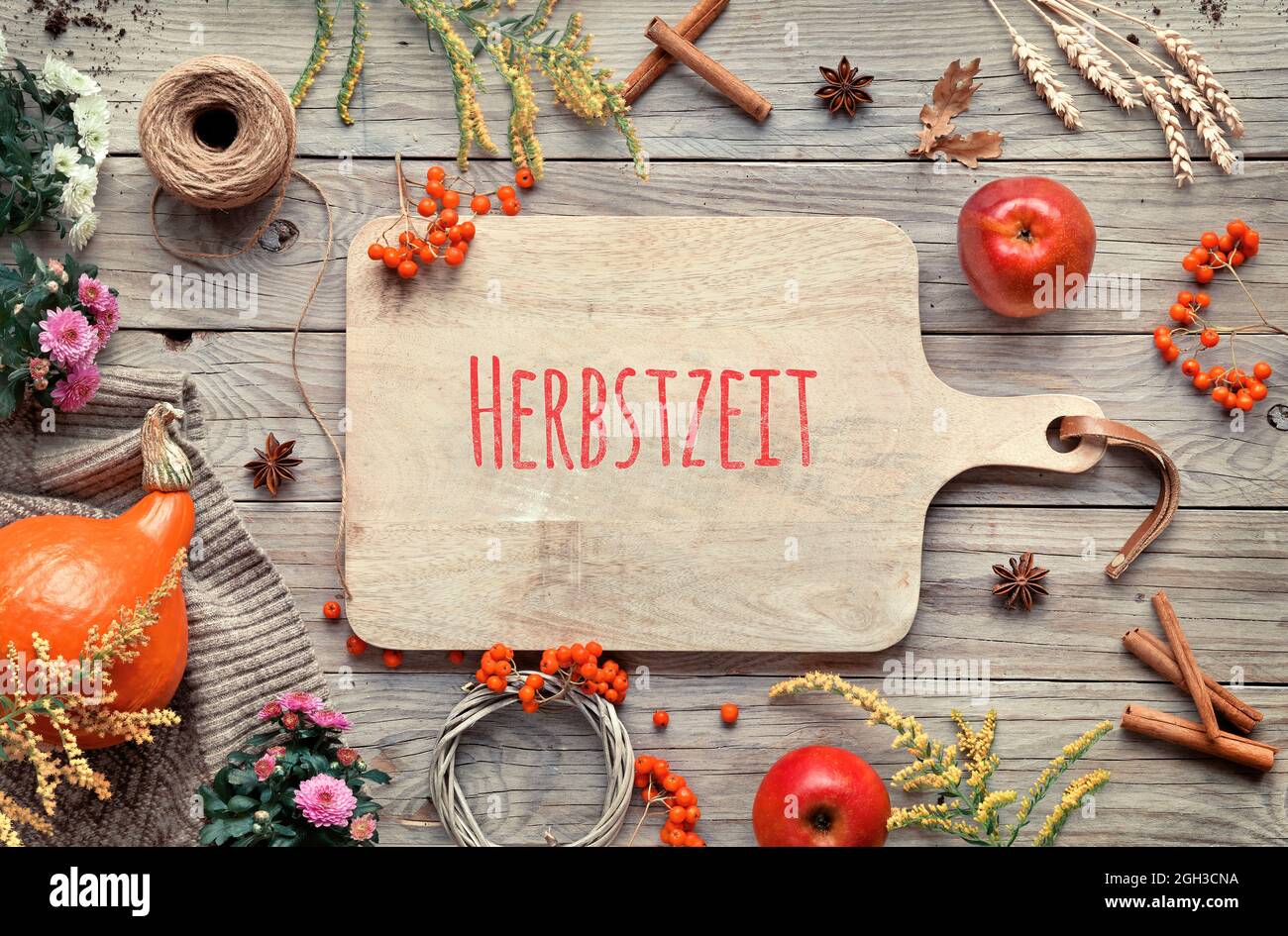 Text Herbstzeit on cutting board means Autumn in German language. Orange pumpkins, rowan berry, apples, cinnamon and frame made from Fall decorations Stock Photo