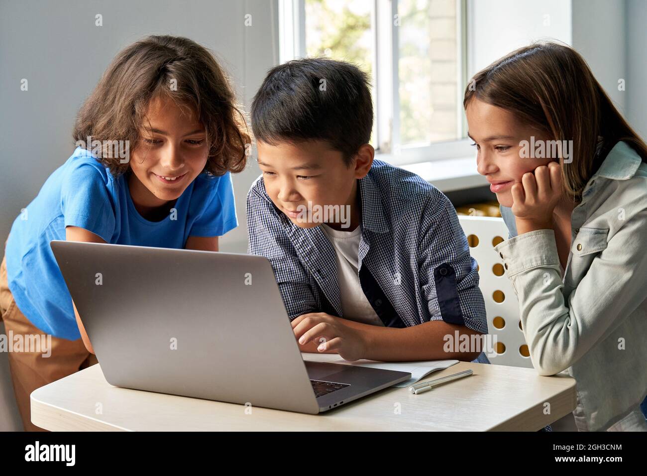 Diverse happy school kids using laptop computer together in classroom. Stock Photo